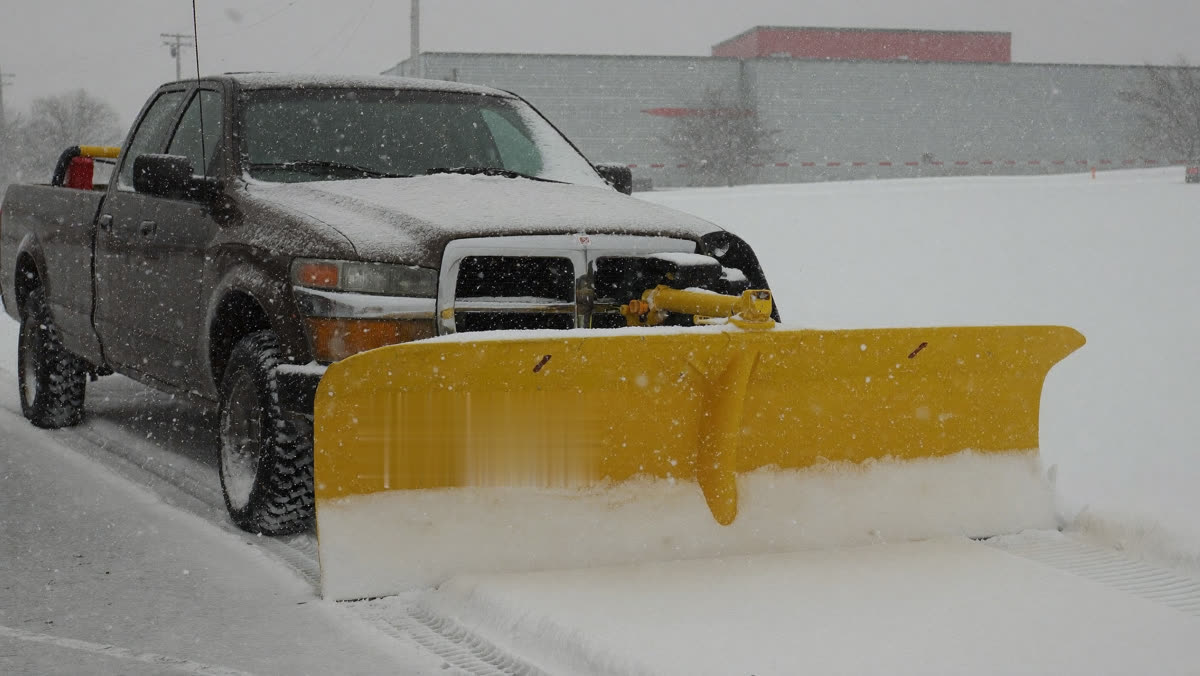 Pickup truck with a plow blade clearing deep snow in a commercial parking lot